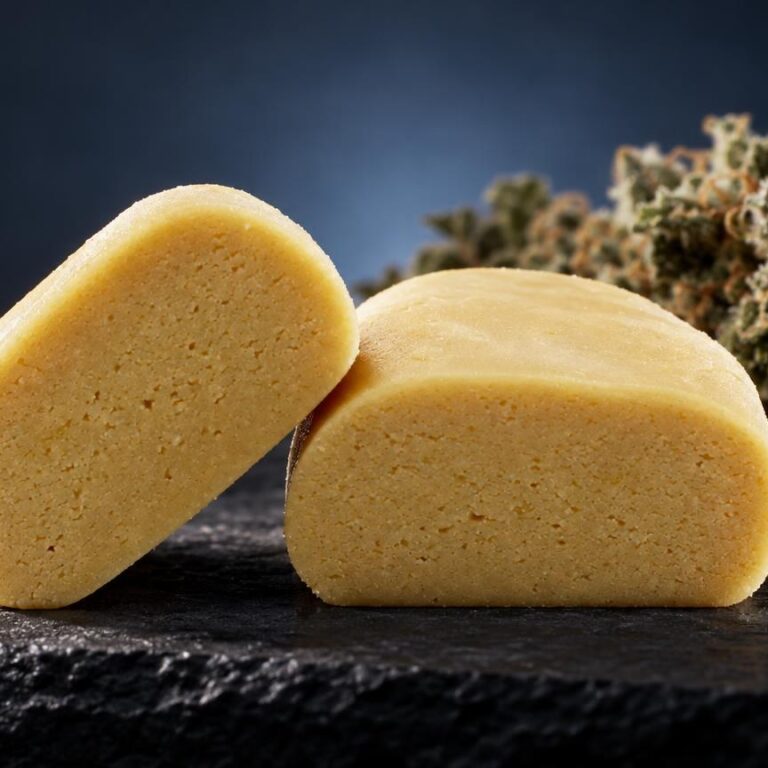 Piatella Hash: zwei hellgelbe, längliche Blöcke mit poröser Textur neben getrockneter Cannabisblüte auf schwarzem Untergrund